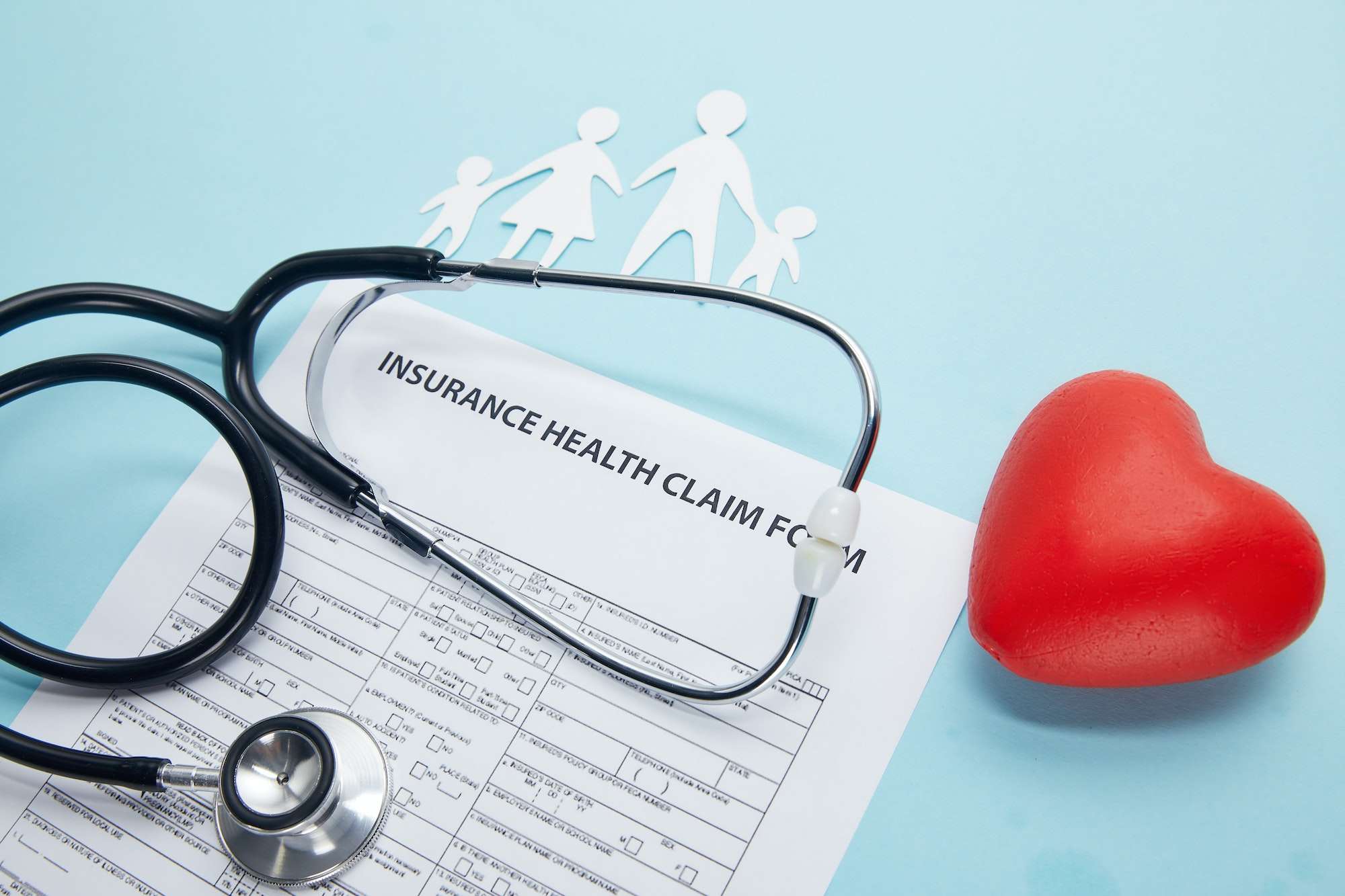 close-up view of insurance health claim form, paper cut family, red heart symbol and stethoscope on